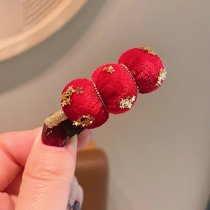 Détail de la pince à cheveux rouge avec pompons en velours et sequins dorés étincelants