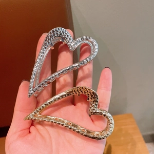 Hand met hartvormige haarklemmen in goud en zilver met een getextureerde gehamerde afwerking