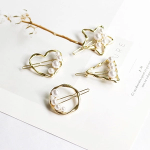 Detail view of four gold-finish metal hair clips with elegant pearls in geometric shapes