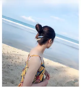 Blue marble and glitter shell hair clips worn by a model against a beach backdrop