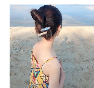 Close-up of sparkling blue and gold seashell hair clips on model's hair at the beach