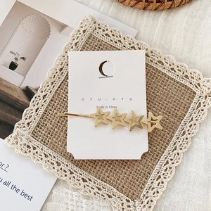 Close-up of golden metal hair clip with four hollow stars on white card with lace decor