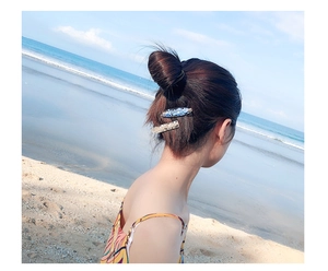 Close-up of blue and beige floral acetate hair clips on a female model with beach background