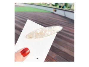 Close-up of a pearlescent white shell hair clip held against an outdoor background