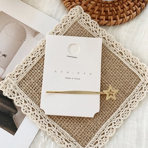 Detail of a minimalist gold star hair clip accessory on a white nYUnYU display card