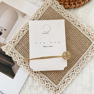Detailed close-up of a Korean gold smiley face hairpin on a display card with a lace background