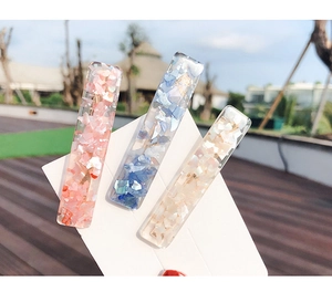 Detailed view of resin hair clips with shell inlay and golden metal base in bright sunlight