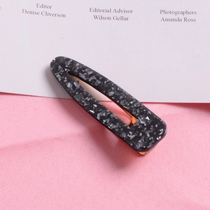 Close-up of marble pattern hair clip with gold metal base on a pink textured background