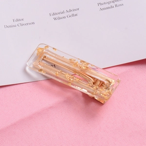 Detail of transparent acrylic hair clip with embedded gold foil flakes on pink fabric