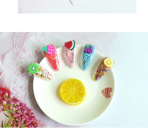 Détail de cinq barrettes à cheveux motifs fruits avec paillettes colorées sur plat céramique