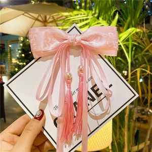Detailed view of elegant pink satin bow hair clip with vintage floral prints and long tassels