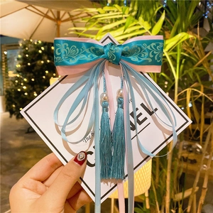 Detail of vintage bow hair clip with cyan tassels and pearls on a branded card