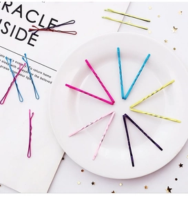 Close-up of vibrant candy-colored metal hairpins arranged on a white ceramic plate