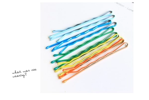 Detail of five colorful wavy metal hair pins in blue green yellow and orange lacquer