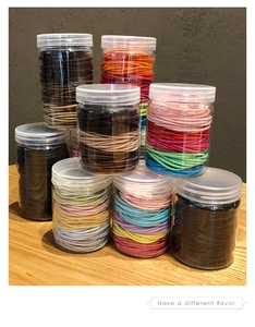 Stack of multi-colored elastic hair ties in transparent storage jars on a wooden table