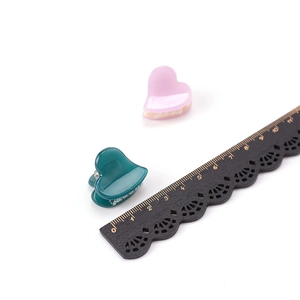 Mini pinces à cheveux cœur vertes et roses présentées avec une règle pour la taille