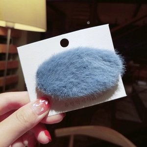 Close-up of a light blue plush faux fur oval hair clip on a retail display card