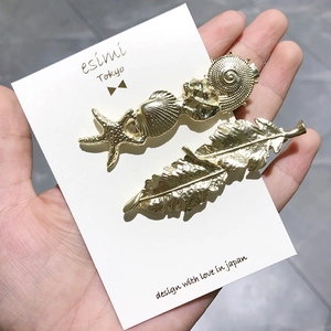 Détail de barrettes dorées avec coquillage, étoile de mer et plume sur carte