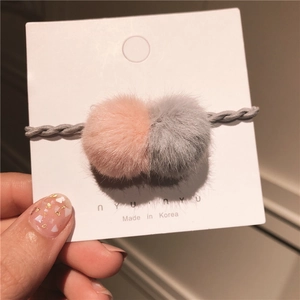 Detail von weichen rosa und grauen Webpelz-Pompons an einem gedrehten Haargummi
