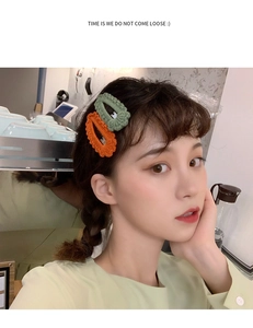 Detail of knitted wave-edge hair clips in green and orange worn by a model