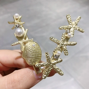 Détail de deux barrettes dorées sur le thème de l'océan avec étoiles de mer et perles