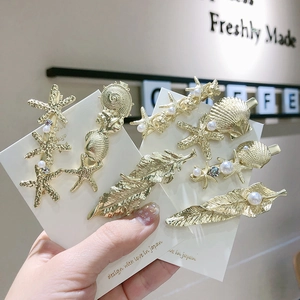 Détail de barrettes dorées sur le thème marin avec étoiles de mer, coquillages et perles