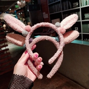 Gros plan d'un serre-tête oreilles de lapin rose avec pompons colorés et peluche