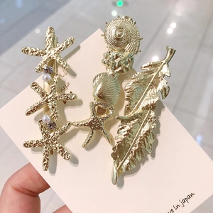 Détail de trois barrettes dorées avec étoiles de mer, coquillages et perles sur une carte