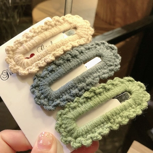 Close-up of three knitted hair clips in beige, blue, and green on a display card