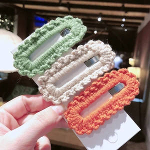 Detail of three knitted wool BB hair clips in green, beige and orange with wave edges
