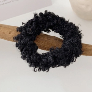 Macro detail of plush black faux lamb wool scrunchie on a natural wooden branch