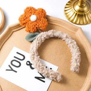 Close-up of soft beige plush headband featuring a large orange floral design on wood