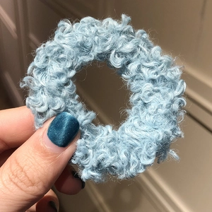 Macro shot of fluffy light blue lamb wool hair scrunchie with soft curly texture