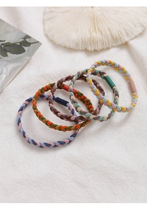 Detail view of five Morandi colored braided elastic hair ties on minimalist white fabric