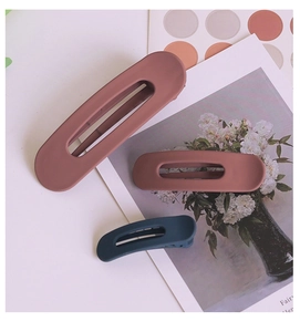 Close-up of three matte hair clips in Morandi colors on a decorative magazine background