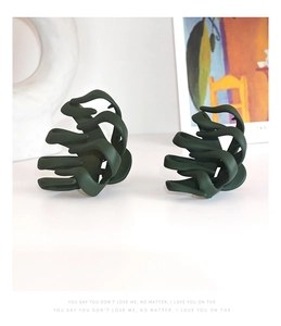 Detail of two dark green matte hair claws with wavy design on a white aesthetic background