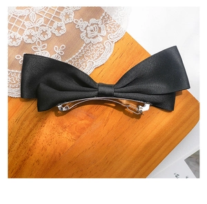 Close-up of black satin bow hair clip with silver metal spring fastener on lace