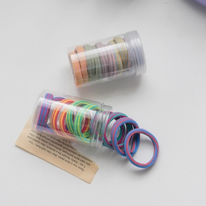Colorful striped elastic hair bands in a clear cylinder container on a white surface