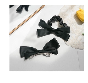Detailed view of elegant black satin bow hair clip and matching scrunchie on a white surface