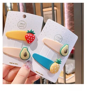 Macro detail of cute strawberry and avocado fruit hair clips on a handmade card display