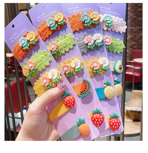 Close-up of handmade crochet flower and fruit hair clips for kids on purple cards