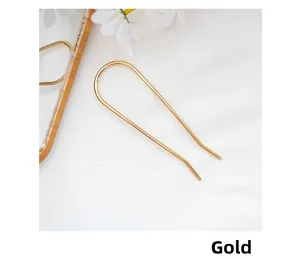 Close-up of minimalist gold U-shaped metal hair pin on elegant white fabric background