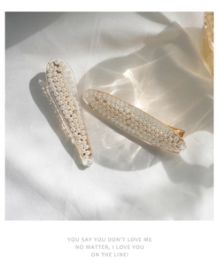 Detailed view of mermaid pearl hair clips with resin and gold metal on white fabric