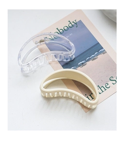 Set of two crescent-shaped hair claws in clear and beige acrylic on a stylish magazine