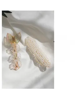 Detailed view of mermaid tail resin clip and white pearl hair clip on white fabric