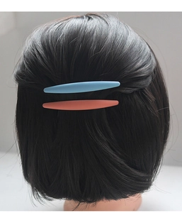 Détail de pinces à cheveux bleu clair et orange mat sur des cheveux foncés