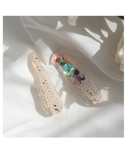 Detail view of pearl and colorful stone mermaid tail hair clips on white silk fabric