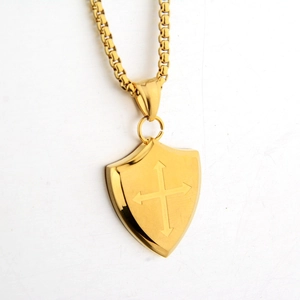 Macro shot of gold shield pendant featuring a cross engraving and sturdy box chain
