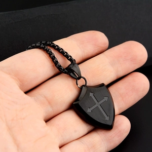 Macro detail of matte black shield pendant with cross motif and brushed steel finish