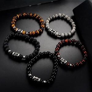 Top view of five natural stone beaded bracelets with vintage silver metal charms on black surface